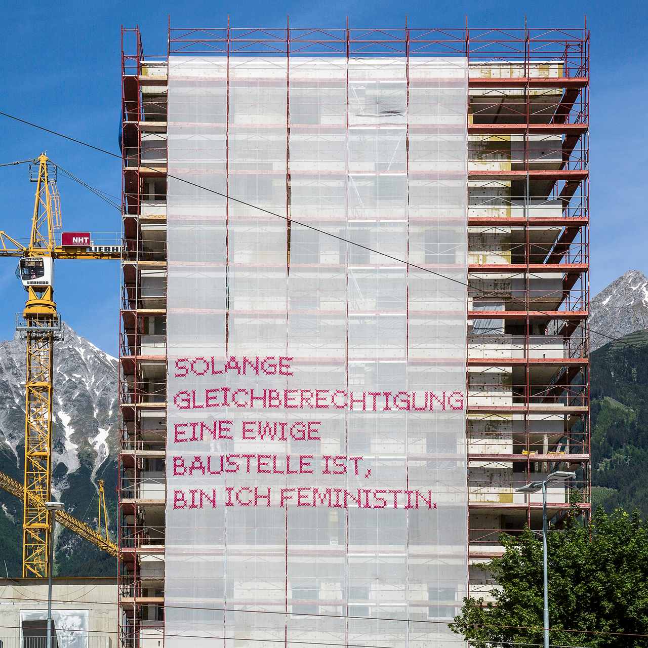 Bild Hochhaus mit besticktem Banner vorne dran. Text: Solange Gleichberechtigung eine ewige Baustelle ist, bin ich Feministin.