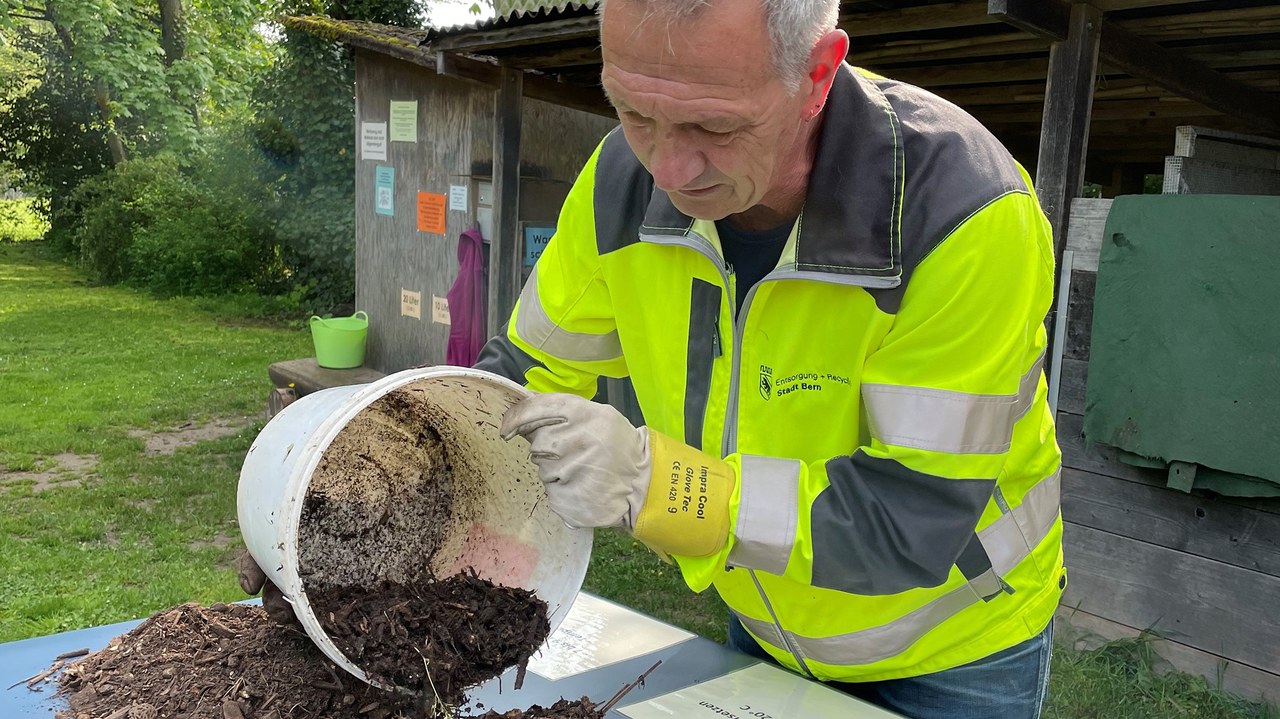 Kursleiter von Entsorgung + Recycling leert Komposterde aus einem Kübel auf einen Tisch.