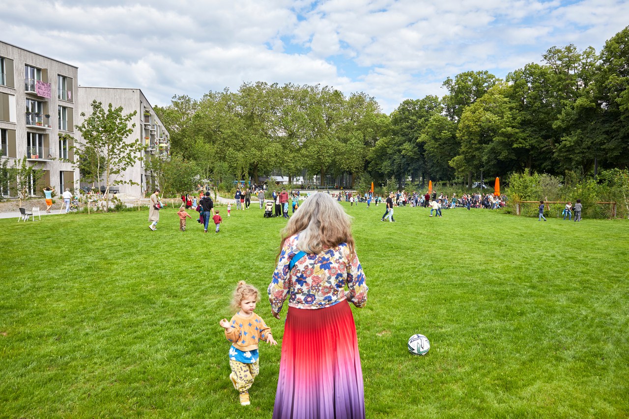 Eine Frau und ein kleines Kind spielen Fussball auf einer grossen Wiese.