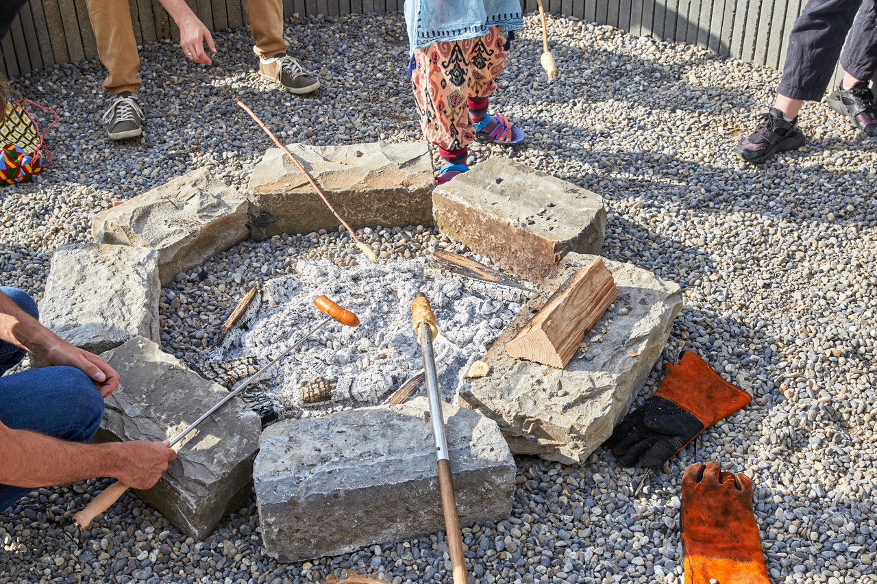 Kinder und Erwachsene bräteln an einer Feuerstelle.